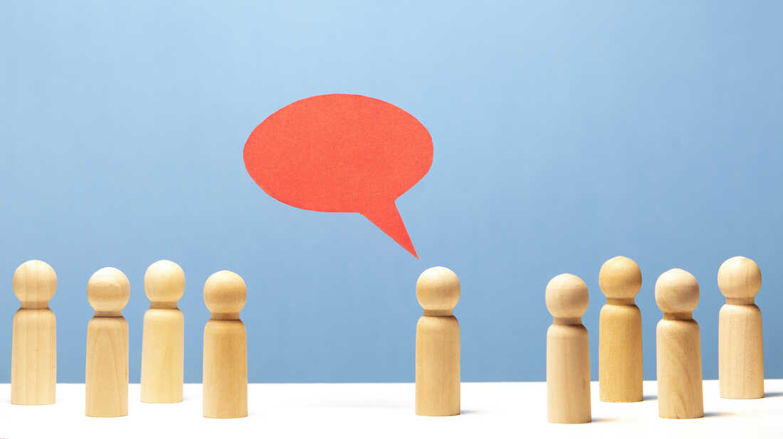 A red speech bubble hangs over a wooden figurine surrounded by 8 other figurines.
